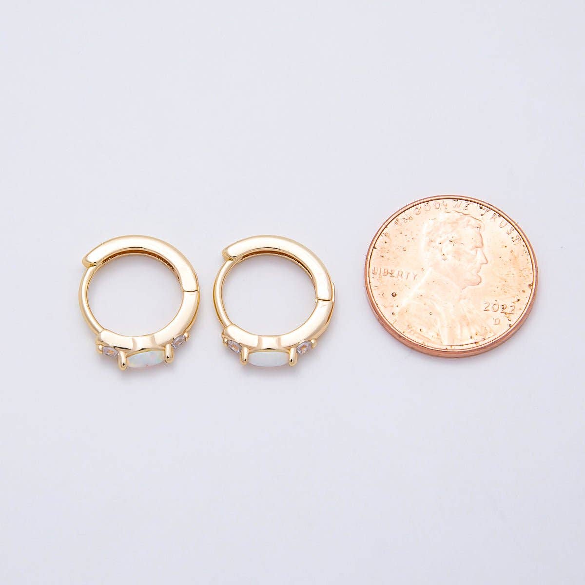 Aim Eternal Gold Filled 13mm White Opal/CZ Huggie Hoops, each set with a white opal and small clear cubic zirconia, shown next to a US penny for scale.