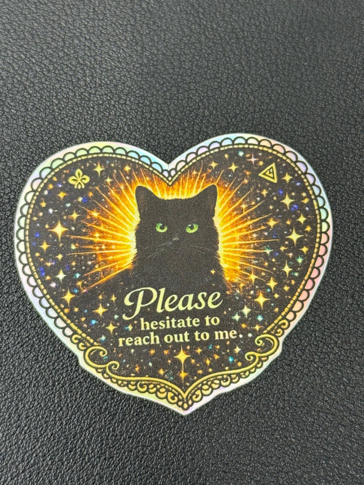Black Cat Holographic “Please Hesitate to Reach Out” Sticker by Hello Brand | Sticker My Art—features a heart-shaped black cat, glowing details, sparkling stars, gold border, and corner symbols. Waterproof vinyl.
