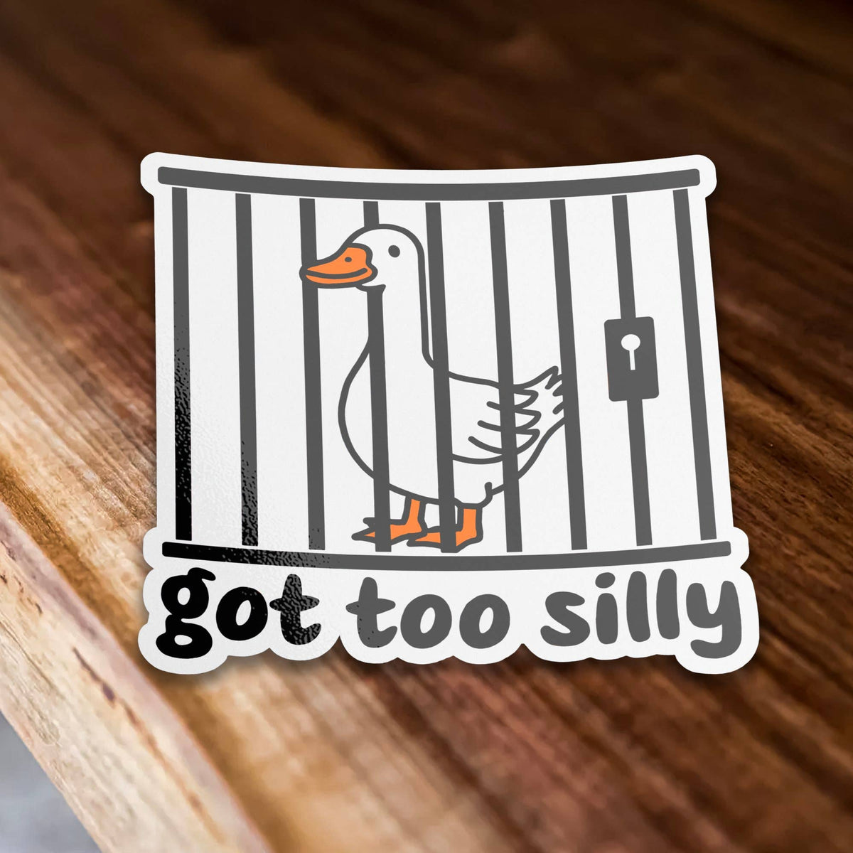 The Got Too Silly Goose Sticker from Sticker Bull features a cartoon goose behind bars over the phrase “got too silly.” This funny sticker is shown on a wooden surface.