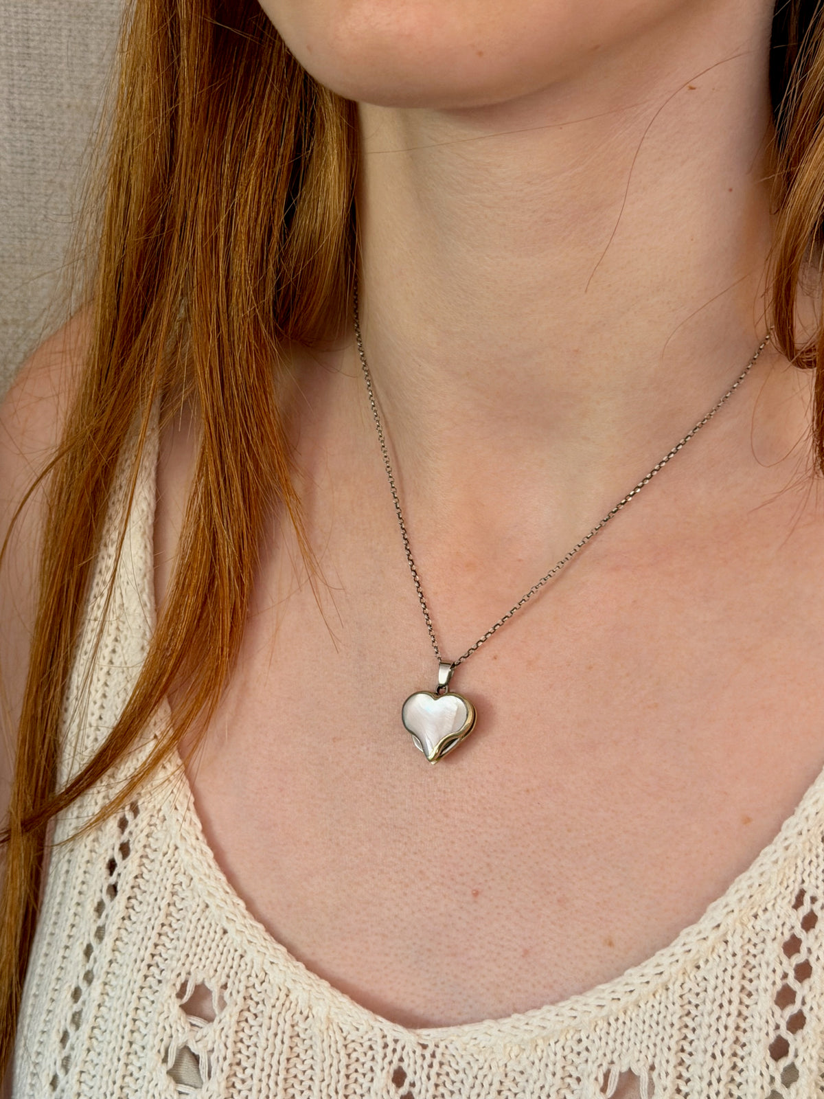 A Blue Ridge Knives Mini Heart Knife Necklace featuring a silver heart-shaped pendant with an abalone shell inlay hanging from a delicate sterling silver curb chain around a person’s neck.