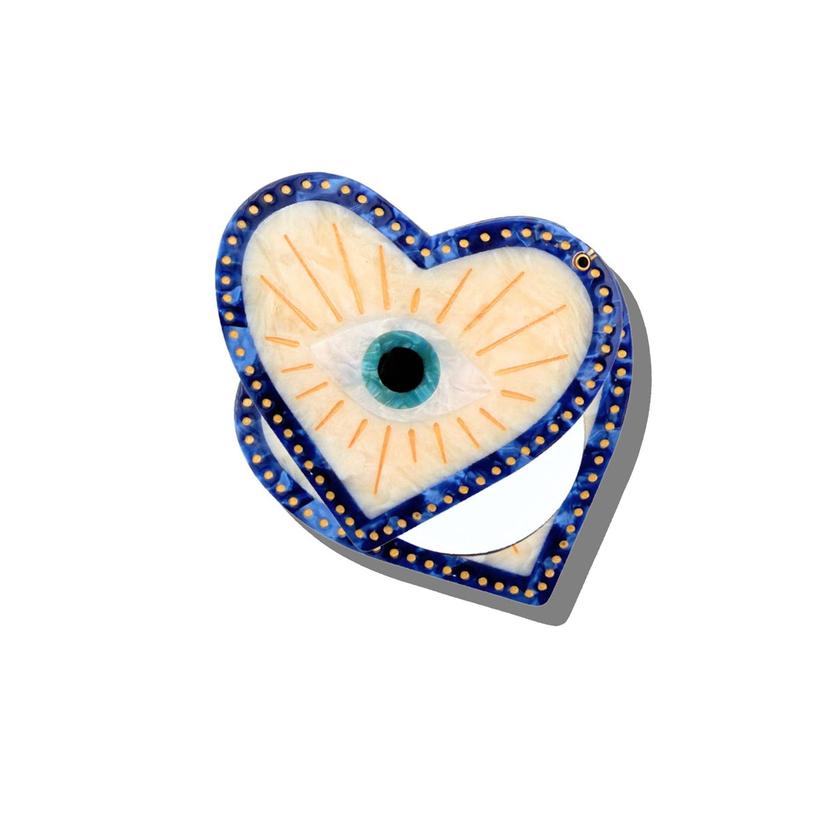 Introducing the Hand-Painted Coastal Lucky Eye Compact Mirror by Solar Eclipse; this heart-shaped compact features a hand-painted design outlined in blue with delicate gold dots.