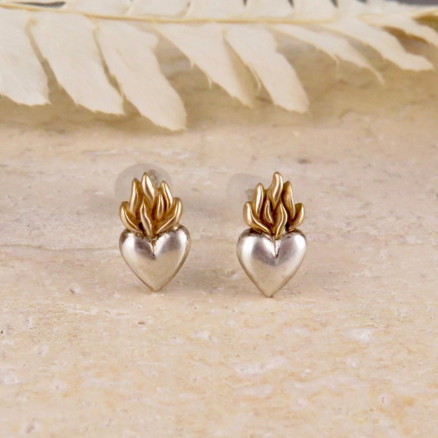 The image shows a pair of small sterling silver heart post earrings with bronze flames design on top
