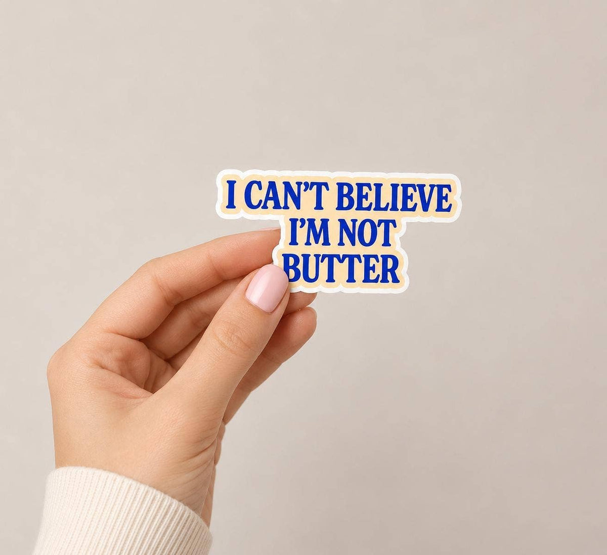 A hand holds an I can’t believe I’m not butter Sticker by Hello Brand | Sticker My Art—matte finish, blue bold letters, neutral background, weather-resistant vinyl.