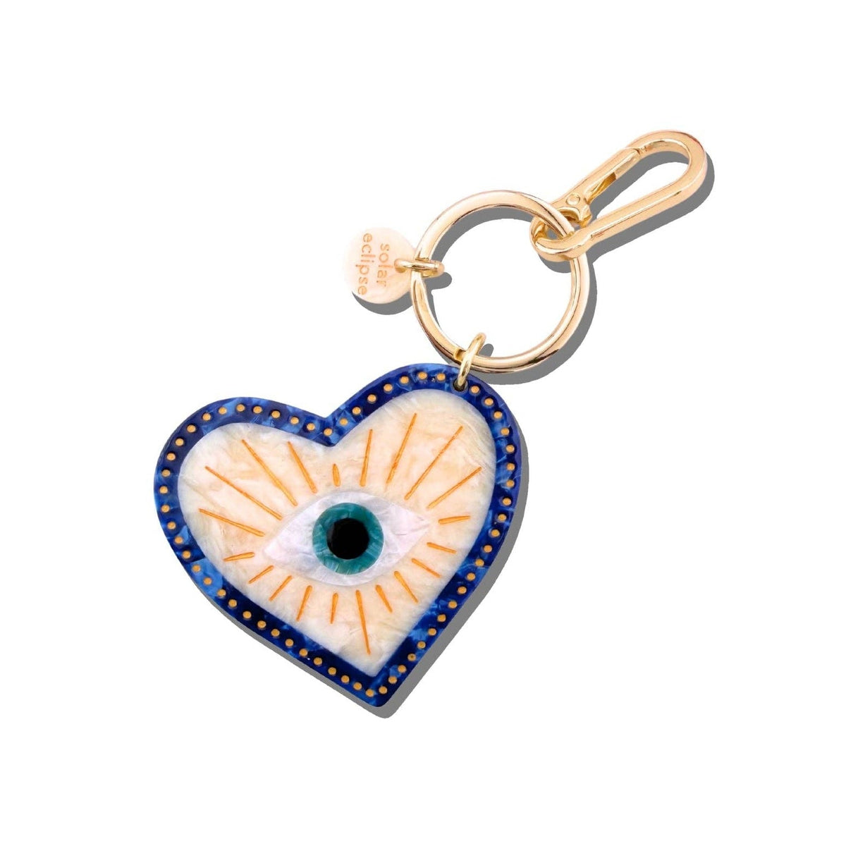 Introducing the Hand-Painted Lucky Eye Bag Charm + Keychain by Solar Eclipse—a heart-shaped accessory featuring a blue and white evil eye at its center, elegantly accented with gold detailing and finished with a gold keyring and clasp.