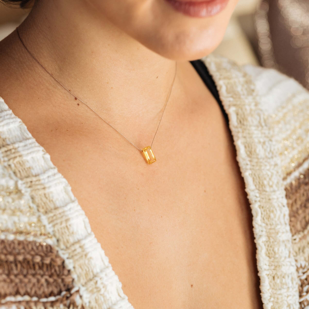 A woman in a textured beige and brown top showcases the SoulKu Citrine Refined Necklace for Manifest, a delicate handmade gold piece with a rectangular pendant that highlights her self-expression.