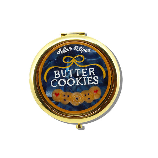 Round gold Butter Cookies Handbag Hero Pill Compact featuring a blue swirled background, the text Solar Eclipse and BUTTER COOKIES, a gold bow icon, and three small cookie illustrations.