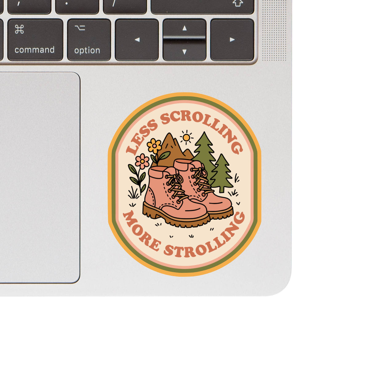 The Less Scrolling, More Strolling Sticker by Juju and Moxie is a 3x2.5″ waterproof vinyl sticker with hiking boots, flowers, and trees, shown on a laptop with the keyboard and trackpad partly visible.