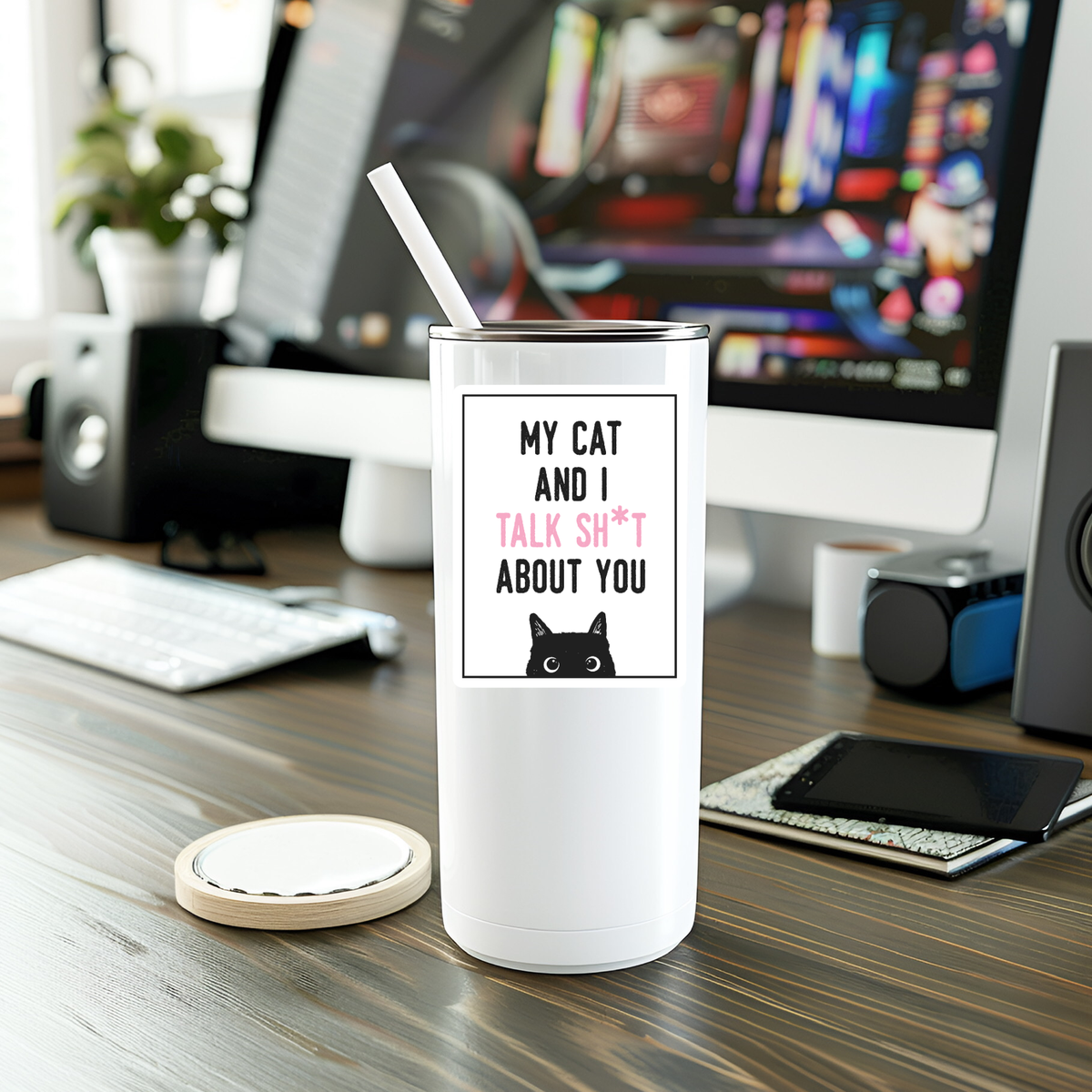 A white tumbler with a straw sits on a desk, decorated with the My Cat And I Talk Sh*t About You Sticker from Mystical Monkey Toes, featuring a black cat graphic. A computer and other desk items are in the background.
