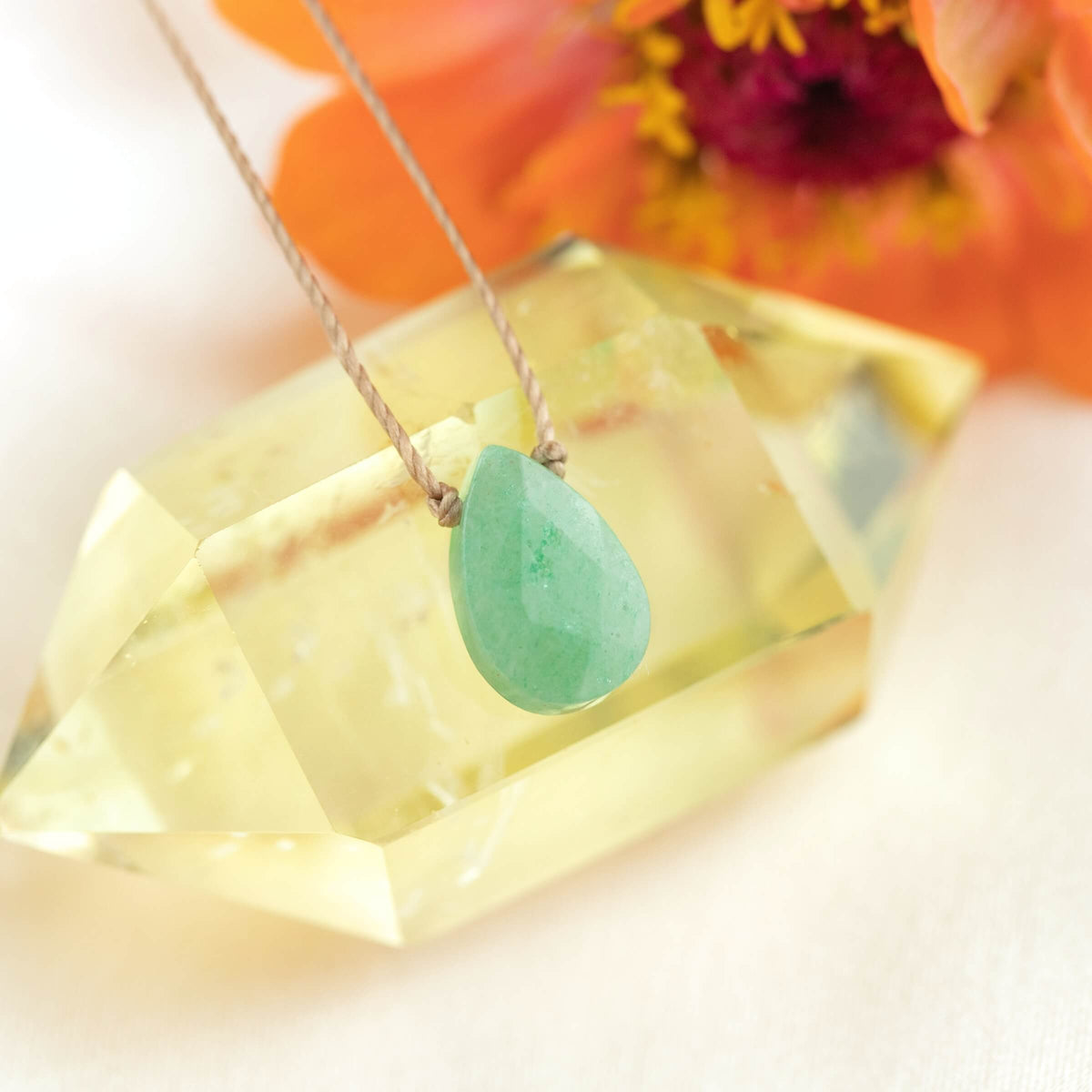 The Green Aventurine Gemstone Necklace - Healing by SoulKu features a handmade teardrop pendant on a cord, displayed on yellow crystal with an orange flower—a unique gemstone jewelry piece.