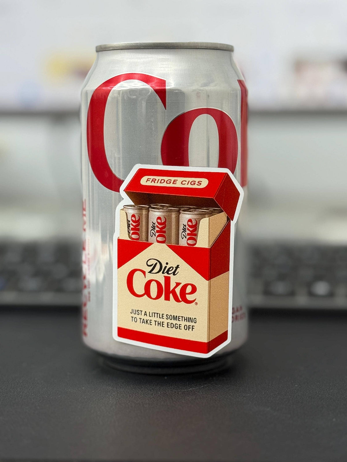 The Diet Coke Fridge Cigs Sticker by Hello Brand | Sticker My Art shows a weather-resistant sticker of a cigarette pack labeled “Fridge Cigs” with mini Diet Coke cans and the phrase “Just a little something to take the edge off.”.