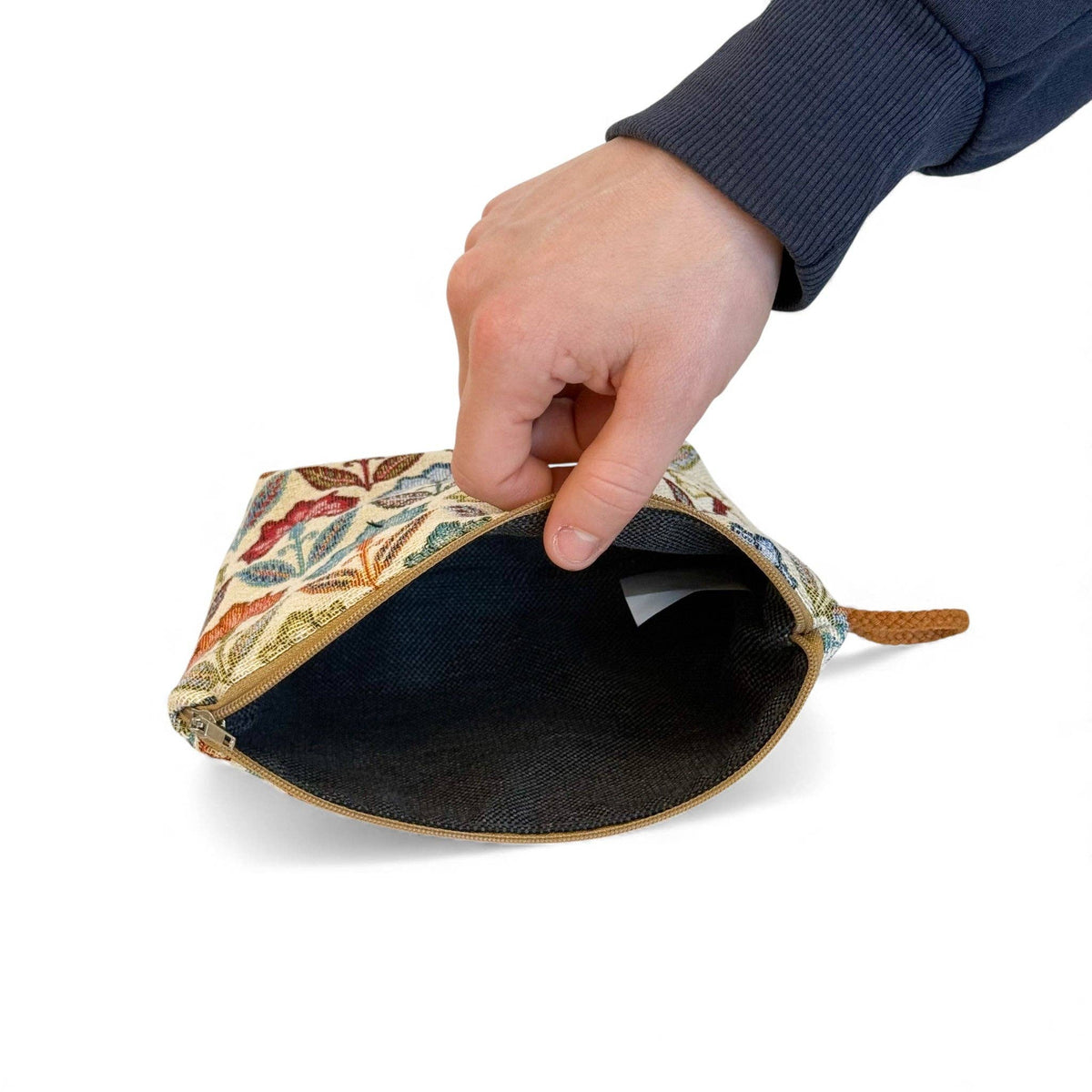 A hand holds open the DE LA MUR LINE US Inc Floral Jacquard Small Makeup Bag – Multicolor (Flora), featuring a colorful floral jacquard pattern on the outside and a dark fabric lining.