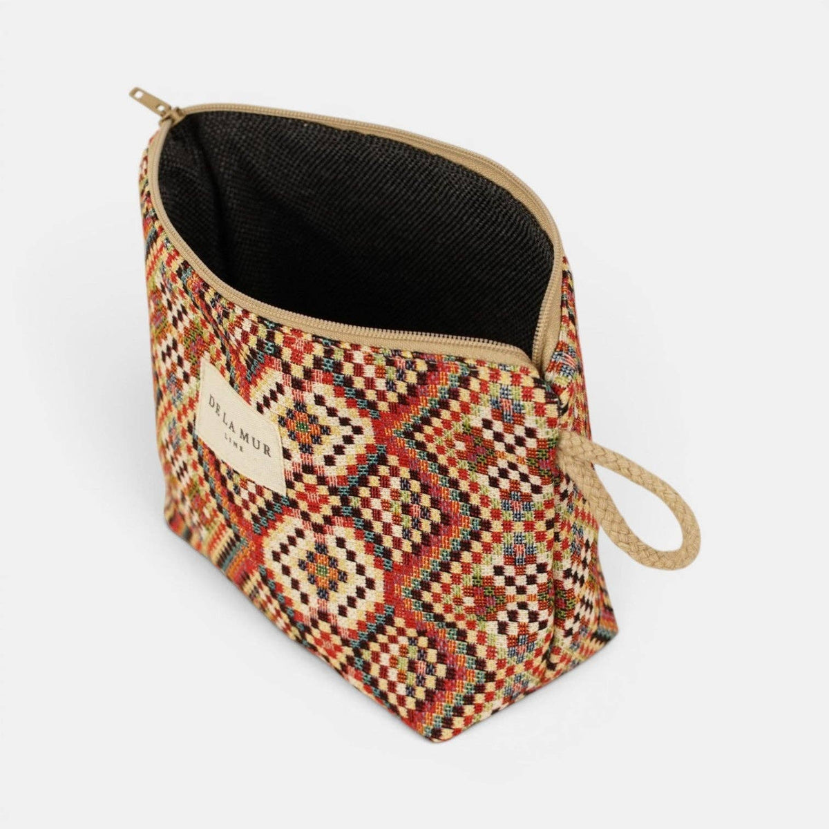 The DE LA MUR LINE US Inc Geometric Jacquard Small Makeup Bag – Red Multicolor (Otto) features a vibrant woven geometric pattern crafted from jacquard fabric, accented with a beige zipper and a handy loop handle. The pouch has a black interior, and the front displays a sewn DELAMUR label. It is shown standing on a white surface.