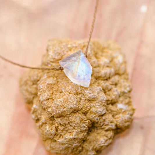 A faceted Moonstone Empowering Necklace for Strong Women on a thin cord, resting on a rough stone.