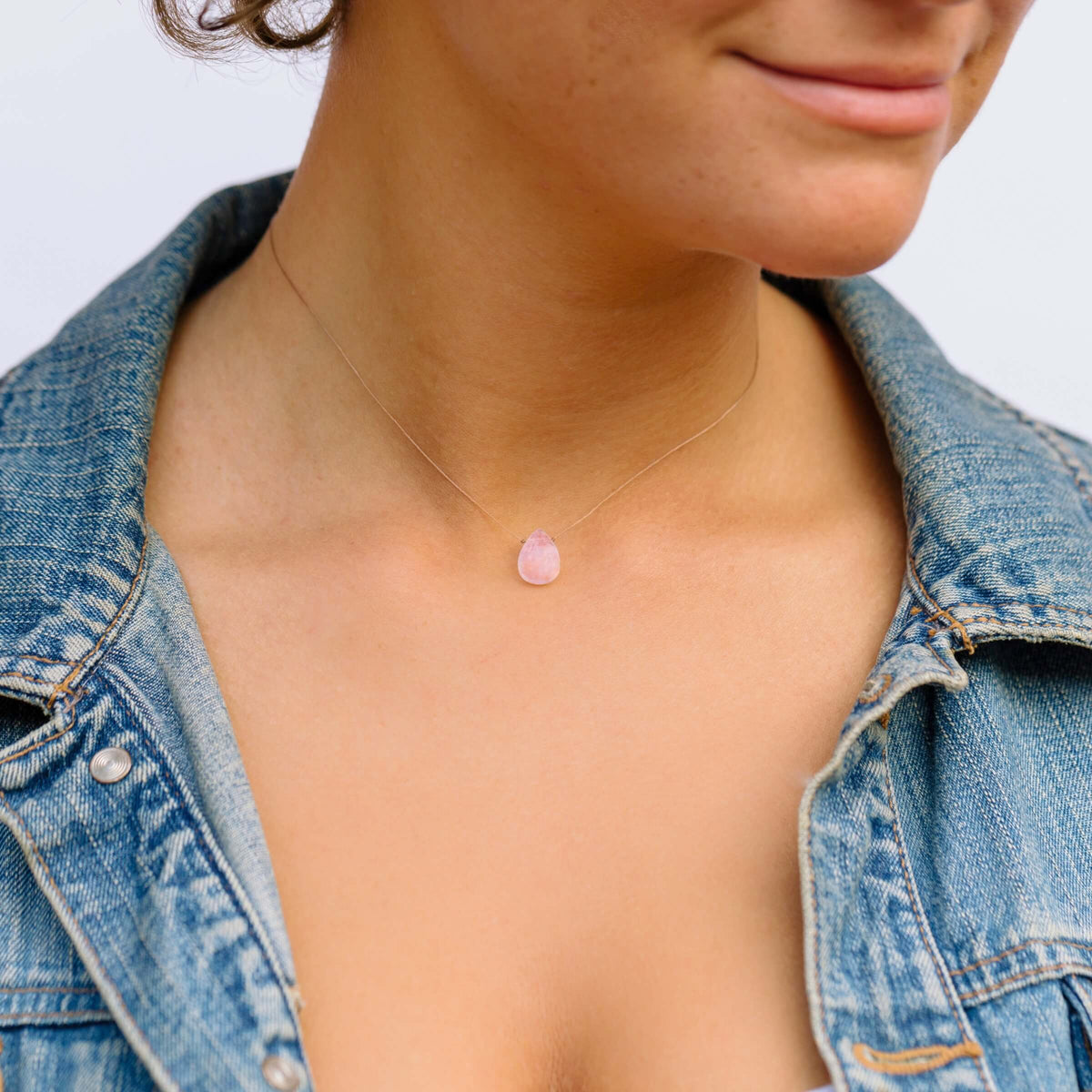 A person wearing the SoulKu Rose Quartz Gemstone Necklace - Love - Dainty Gift Women with a blue denim jacket, shown from the shoulders up, and a slight smile visible.