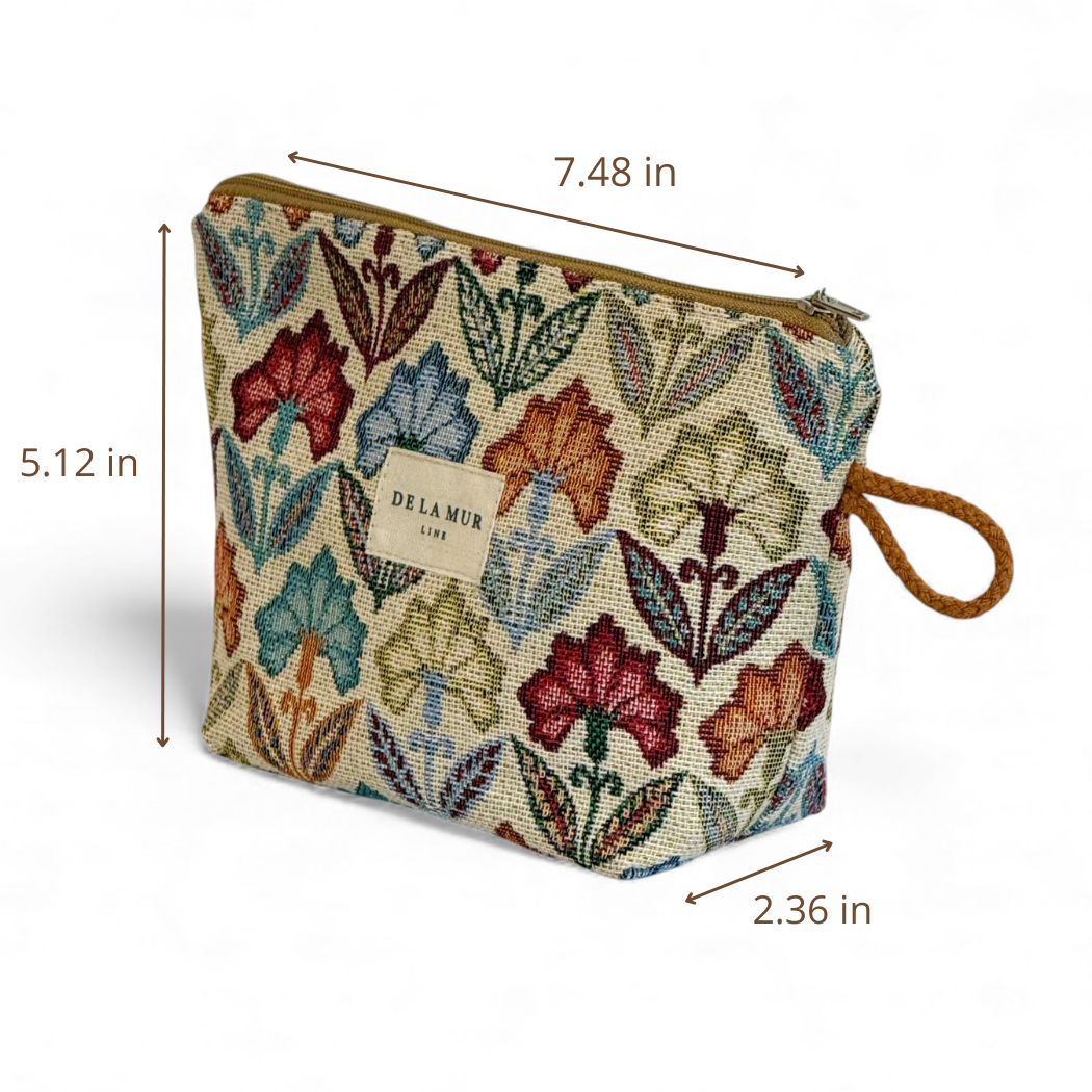 Introducing the Floral Jacquard Small Makeup Bag – Multicolor (Flora) by DE LA MUR LINE US Inc. This rectangular pouch showcases vibrant floral patterns on jacquard fabric, complemented by a tan zipper and a brown loop handle. Designed as a compact makeup bag, it measures 7.48 inches wide, 5.12 inches tall, and 2.36 inches deep. The front features the signature DE LA MUR brand label.