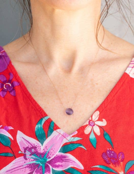 A person in a red floral top wears the SoulKu Iolite Beam Necklace for ‘I Believe in You,’ with loose hair strands and part of the necklace partially out of frame.