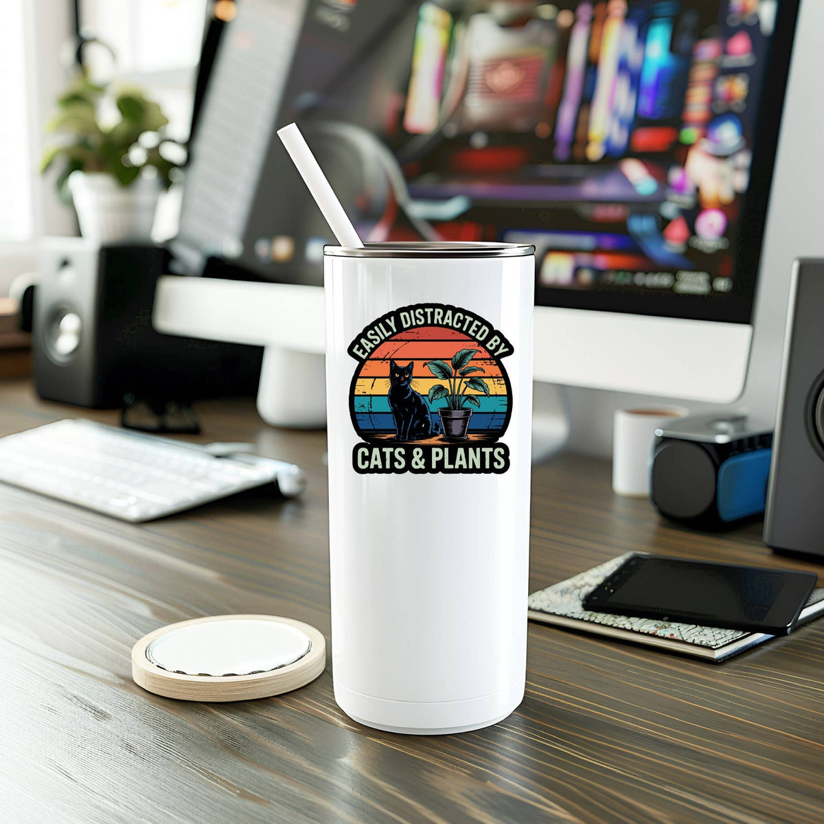 A white tumbler with a straw sits on a desk in front of a computer, decorated with the Mystical Monkey Toes Easily Distracted By Cats & Plants Vinyl Sticker featuring adorable cat and plant illustrations.