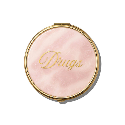 Solar Eclipse Pink Drugs Handbag Hero Pill Compact featuring a round gold-rimmed case with a pink marbled lid and the word Drugs in gold script.
