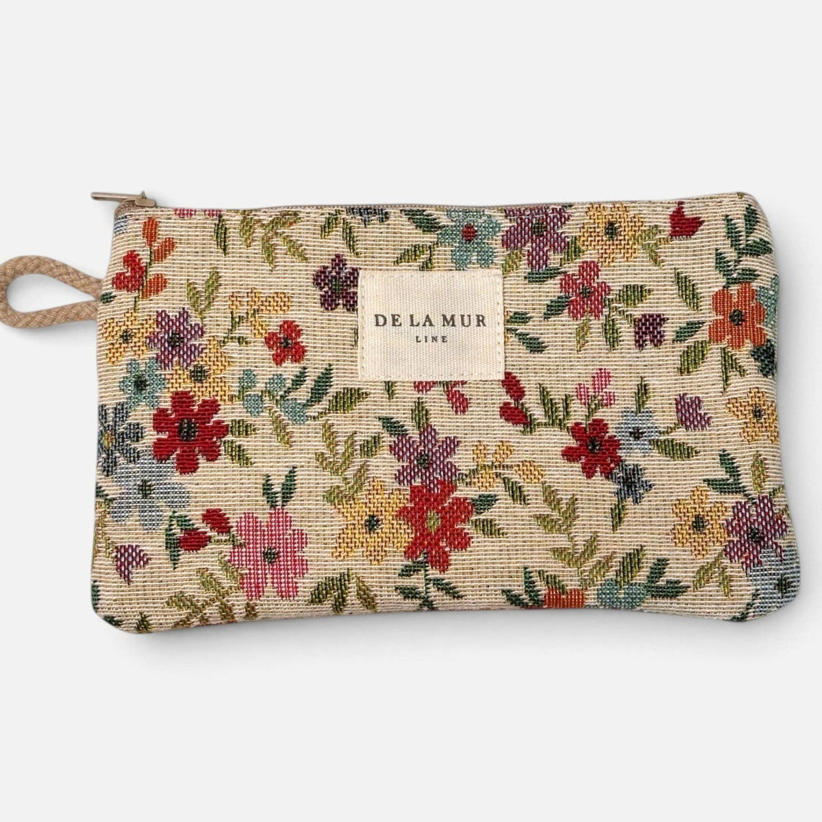 The Floral Jacquard Small Makeup Bag / Coin Purse – Beige (Blum) by DE LA MUR LINE US Inc features a rectangular beige pouch adorned with a vibrant floral jacquard pattern, zipper closure, side loop, and a center-sewn DE LA MUR label. Ideal as a small makeup bag or coin purse.