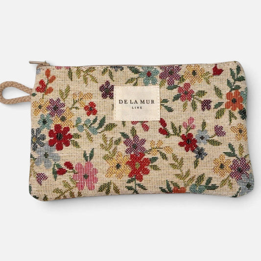 The Floral Jacquard Small Makeup Bag / Coin Purse – Beige (Blum) by DE LA MUR LINE US Inc features a rectangular beige pouch adorned with a vibrant floral jacquard pattern, zipper closure, side loop, and a center-sewn DE LA MUR label. Ideal as a small makeup bag or coin purse.