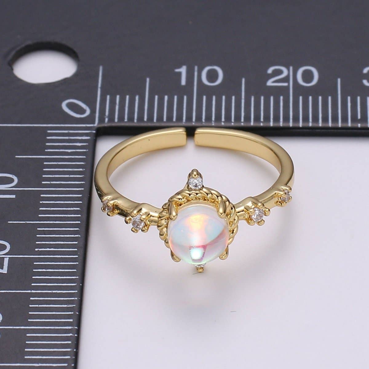 Aim Eternal Opalescent Moonstone Gem Ring GF - Adjustable featuring a gold adjustable band, a central iridescent oval moonstone, and small clear accent stones next to a measuring ruler.