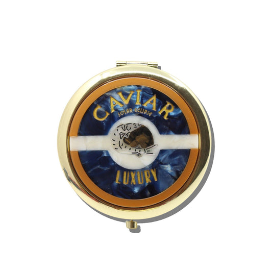 A gold, round, vintage-inspired Solar Eclipse Caviar Handbag Hero Pill Compact - Hand-Painted featuring a blue and white swirled inlay with a central fish illustration, reading CAVIAR at the top and LUXURY at the bottom.