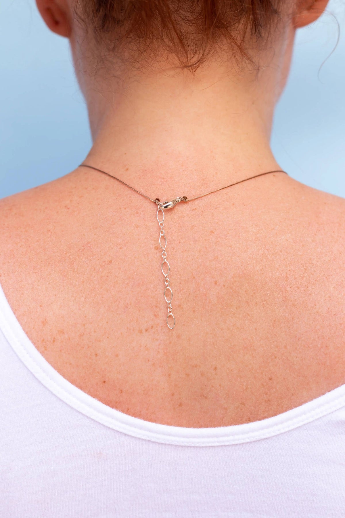 A close-up of a person’s upper back in a white top, showcasing the SoulKu Smoky Quartz Refined Necklace for Release, with the chain draped elegantly down their skin.