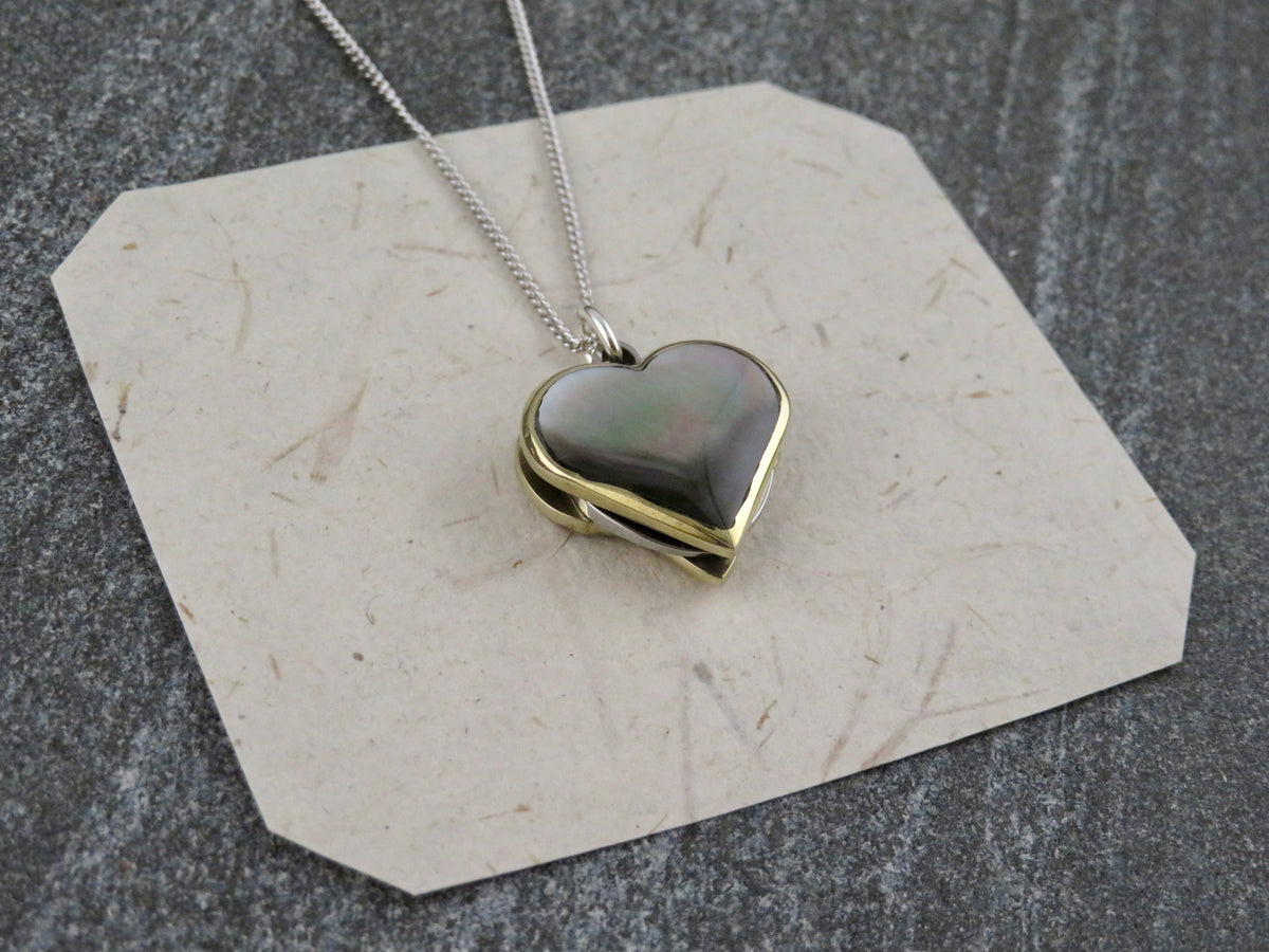 A Mini Heart Knife Necklace by Blue Ridge Knives, featuring a heart-shaped pendant on a sterling silver curb chain with an iridescent abalone shell inlay and a brass border.