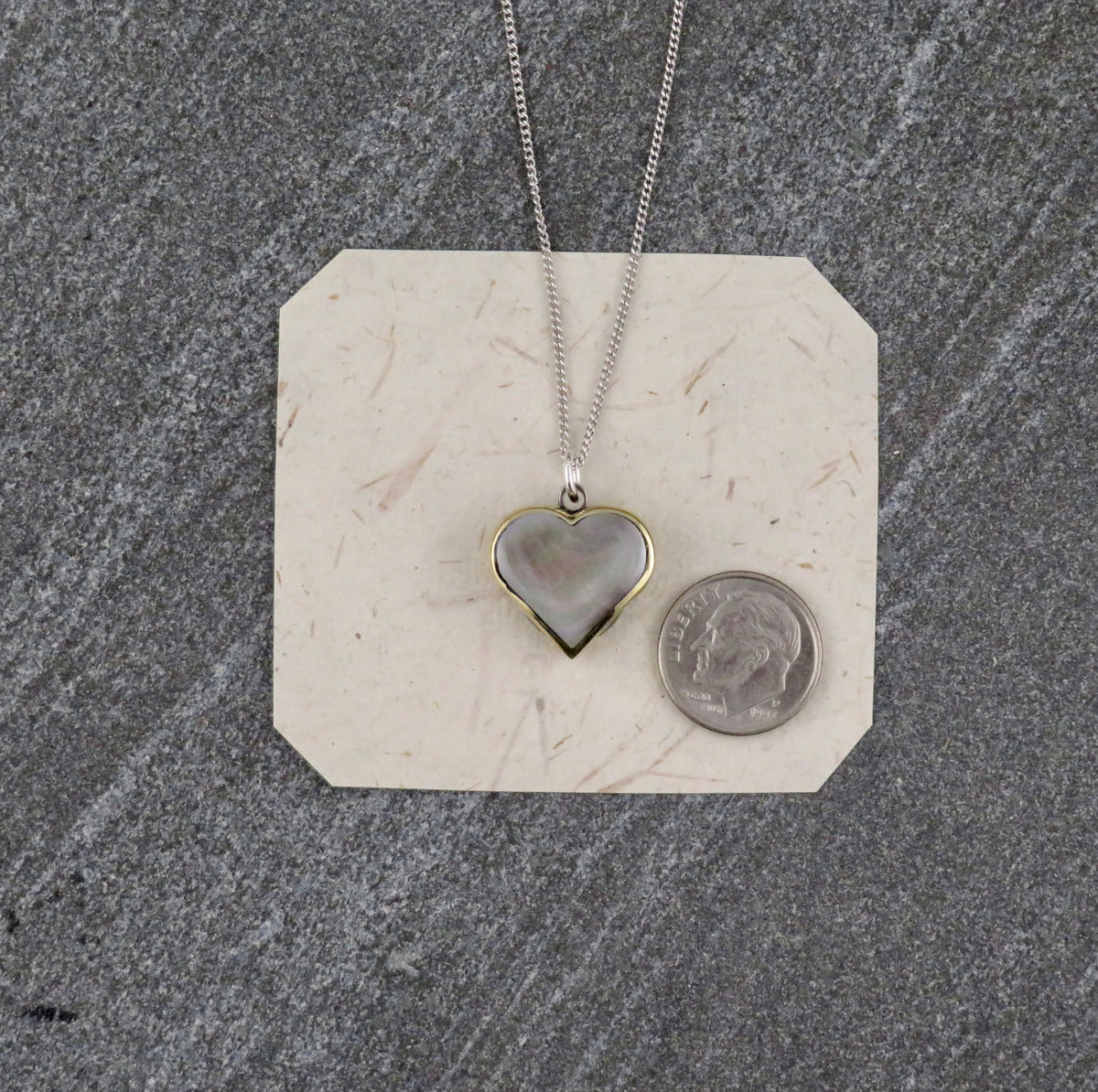 Mini Heart Knife Necklace featuring an abalone shell inlay heart-shaped pendant on a sterling silver curb chain, displayed next to a US dime for scale.
