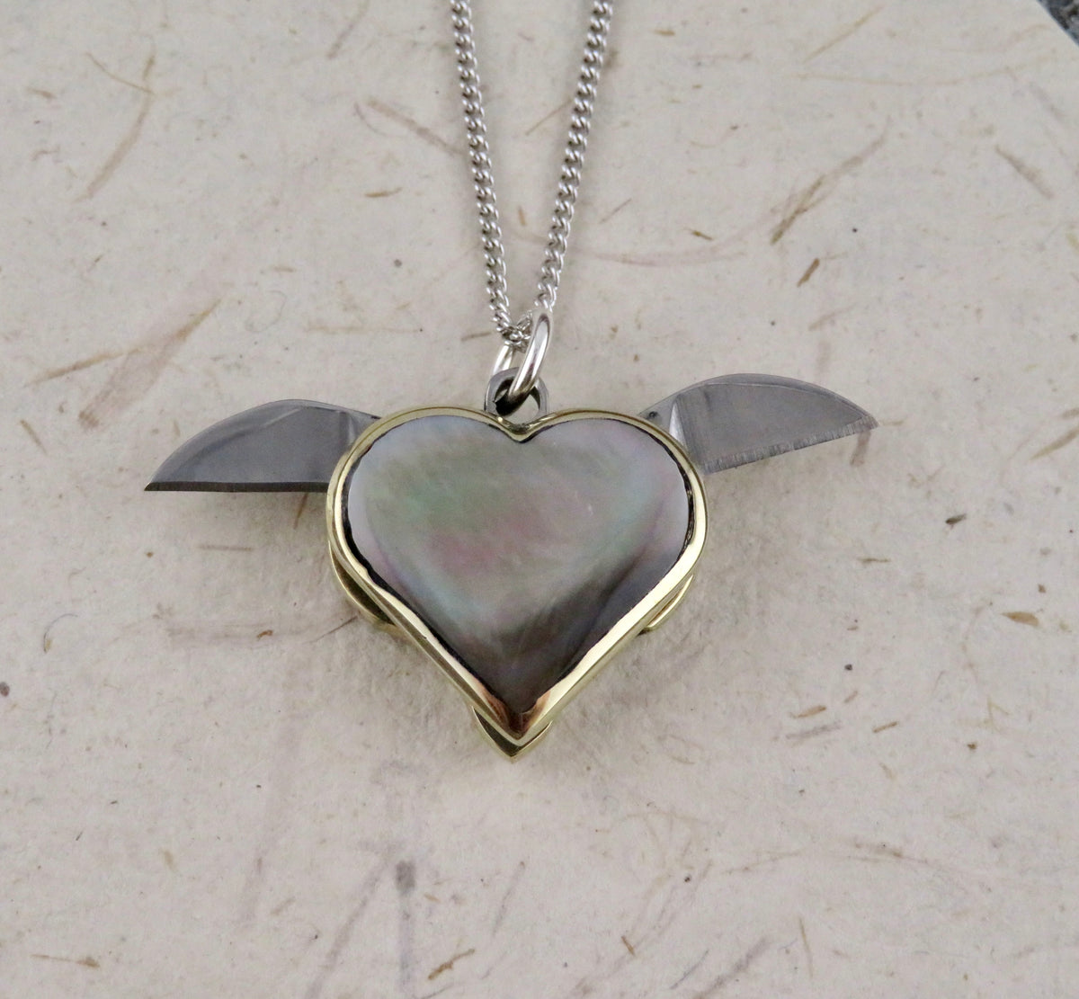 A Blue Ridge Knives Mini Heart Knife Necklace featuring a heart-shaped knife pendant with an abalone shell inlay and two small blades extending from the sides, hanging from a thin sterling silver curb chain.