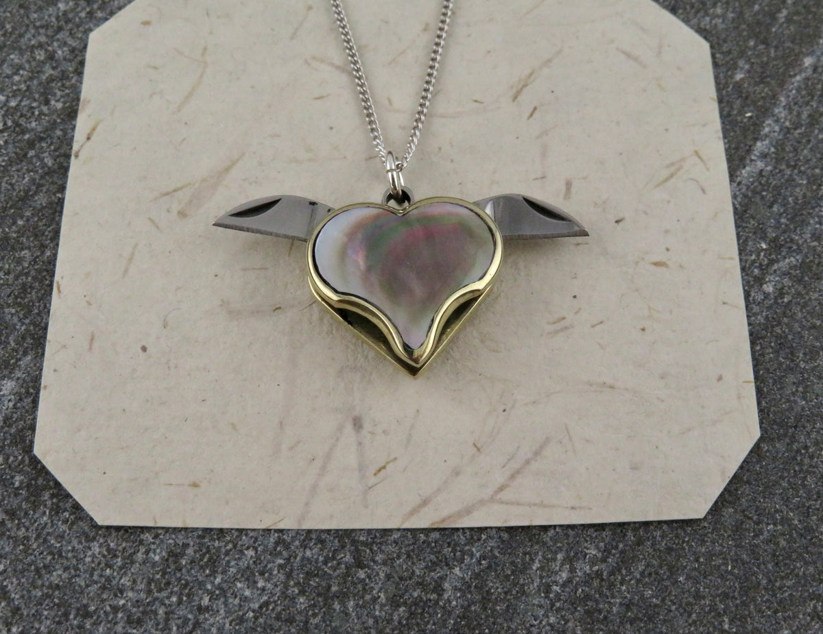 Blue Ridge Knives Mini Heart Knife Necklace featuring an iridescent abalone shell inlay and two small, outward-pointing knife blades on a sterling silver curb chain.