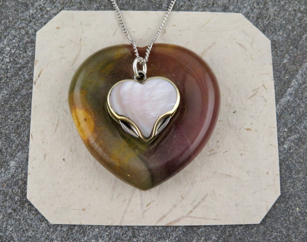 Blue Ridge Knives Mini Heart Knife Necklace featuring a heart-shaped pendant with a white abalone shell inlay, layered over a larger, mottled brown and green heart-shaped stone on a sterling silver curb chain.