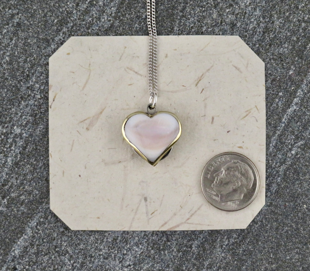 Mini Heart Knife Necklace with an abalone shell inlay heart-shaped pendant on a sterling silver curb chain, shown next to a US dime for scale.