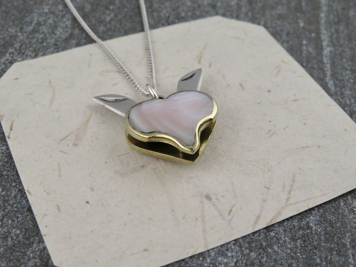 A Mini Heart Knife Necklace featuring a heart-shaped pendant with an abalone shell inlay and two small metal blades extending from the sides, hanging on a sterling silver curb chain.