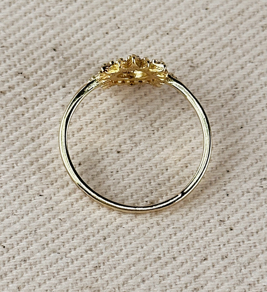 The GoldFi Gold Filled CZ Open Starburst Ring features an intricate, textured design on top and is beautifully displayed on a cream-colored, textured fabric background.