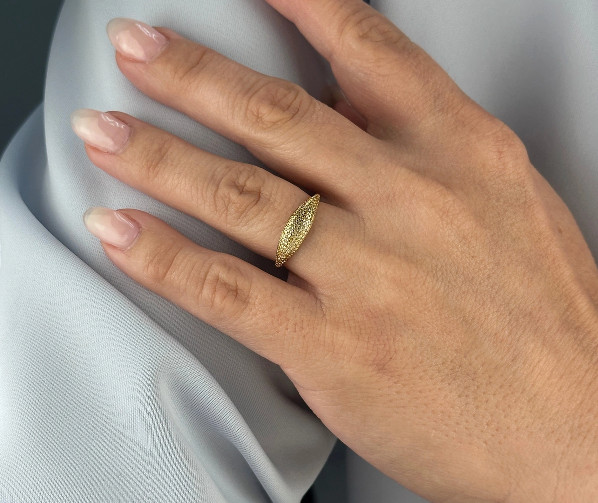 A hand with neatly manicured nails wears the GoldFi Gold Filled Dome Mini CZ Ring on the middle finger, resting on light gray fabric.