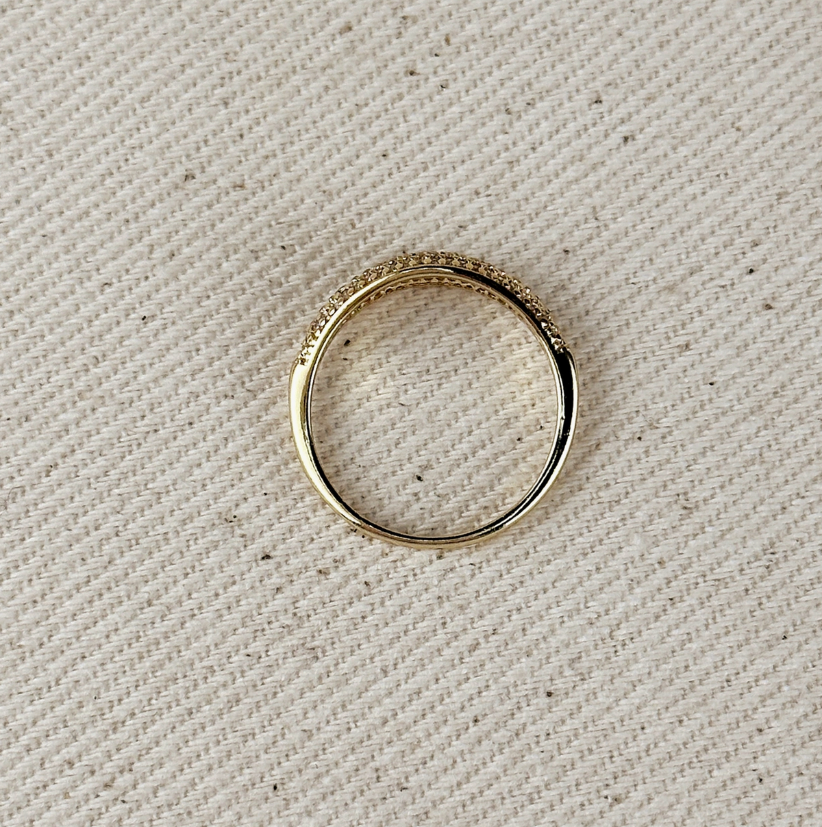 The GoldFi Gold Filled Dome Mini CZ Ring, featuring small sparkling pave stones on one side, is displayed on a textured beige fabric background.
