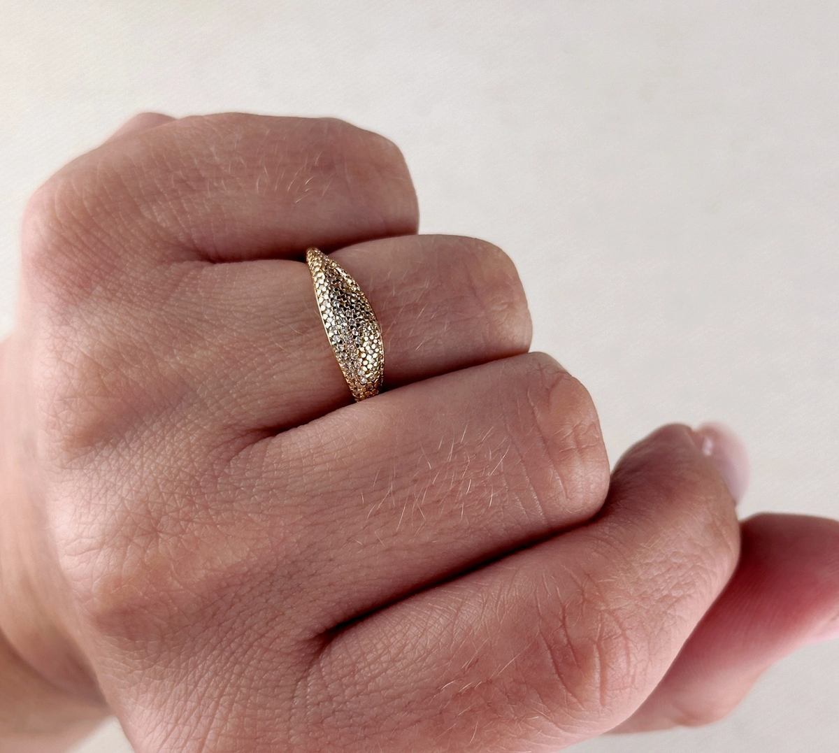 A hand adorned with the GoldFi Gold Filled Dome Mini CZ Ring, featuring a textured, elongated oval design and sparkling cubic zirconia on the middle finger, against a light background.