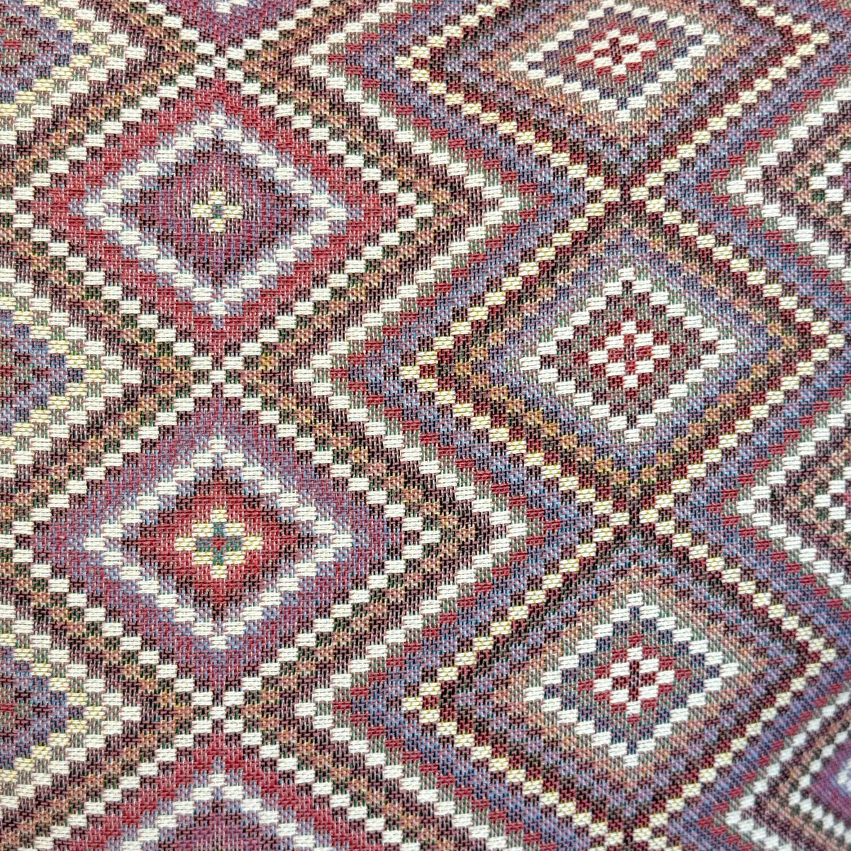 A close-up of the Geometric Jacquard Coin Purse – Pink & Lilac (Nana) by DE LA MUR LINE US Inc shows its intricate jacquard fabric, featuring repeating diamond patterns in soft pink and lilac hues. The diamonds are detailed with small geometric shapes and fine stitching, echoing a classic kilim-inspired design crafted with exceptional detail.