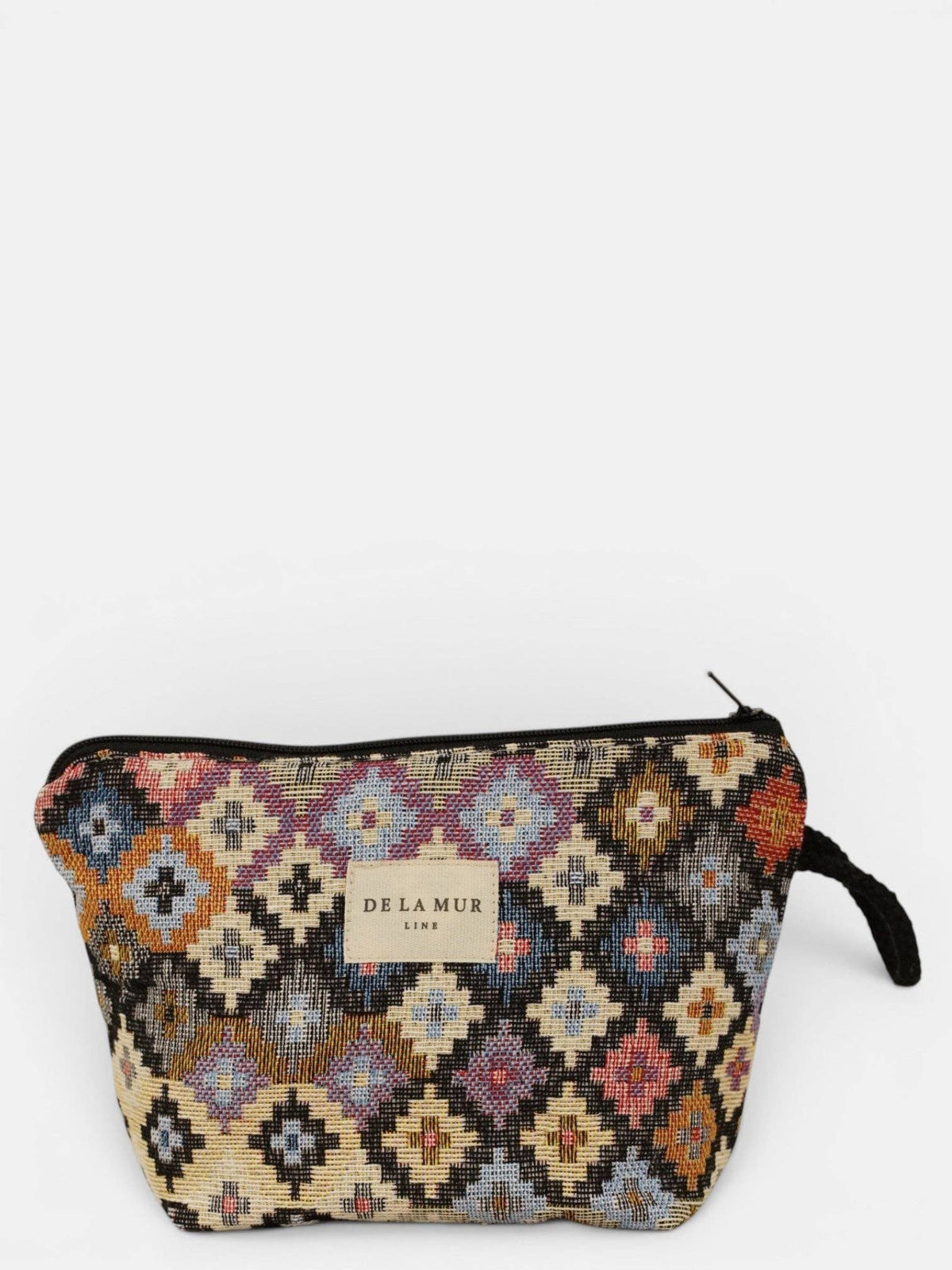 The Geometric Jacquard Small Makeup Bag – Multicolor (Ore) by DE LA MUR LINE US Inc features a vibrant geometric pattern woven from jacquard fabric, a black zipper closure, and a small right-side handle. The front is adorned with a DE LA MUR LIMA label.