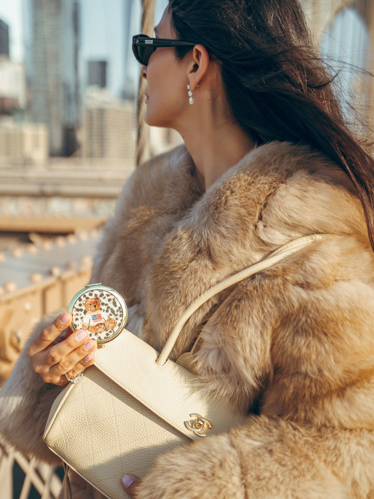 A hand holding a round Teddy Bear Americana Handbag Hero Pill Compact featuring a hand-painted teddy bear wearing a sweater with an American flag design.