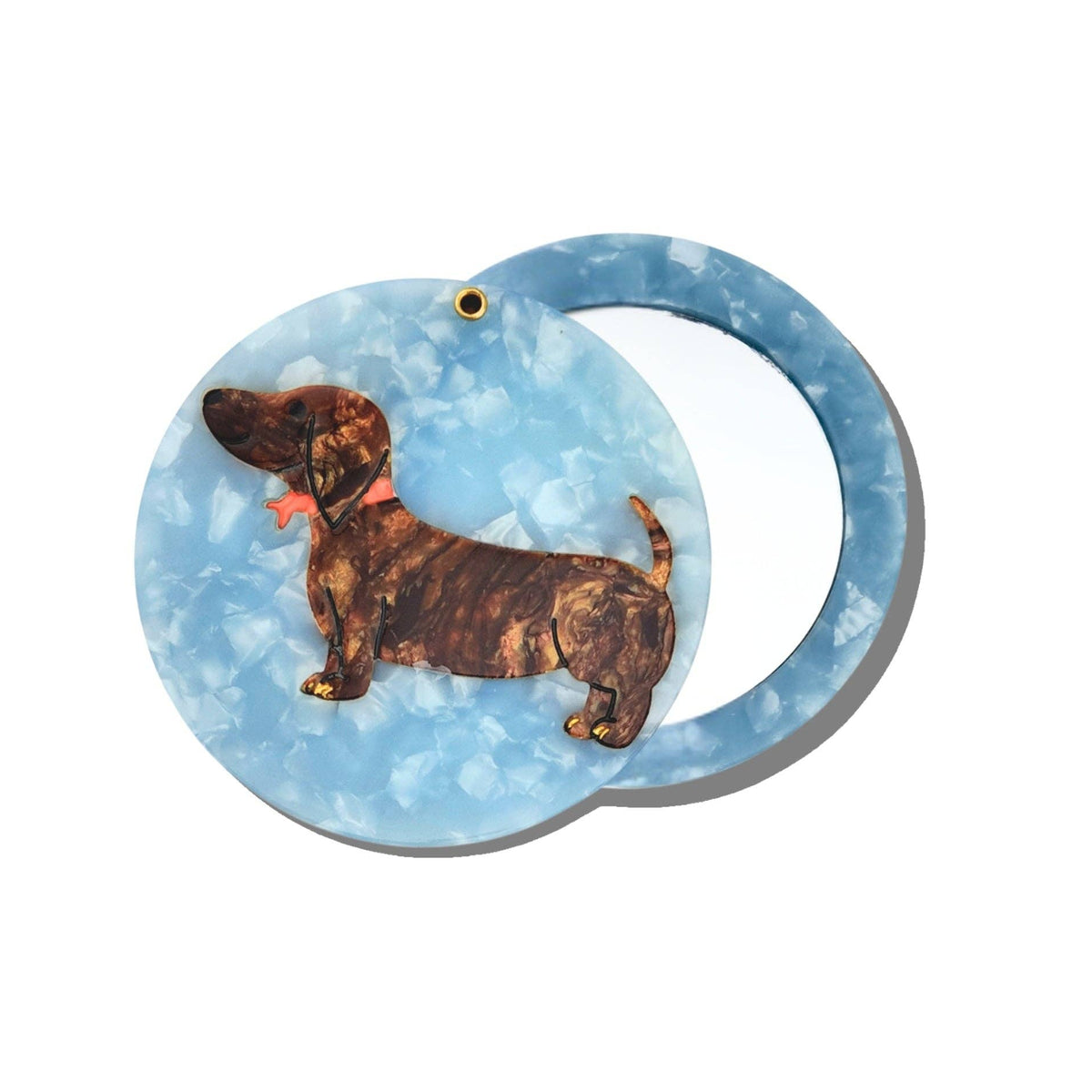 The Solar Eclipse Hand-Painted Dachshund Compact Mirror features a blue cover adorned with a hand-painted brown dachshund sporting a red bow tie. The compact is shown partially open, displaying the interior mirror.