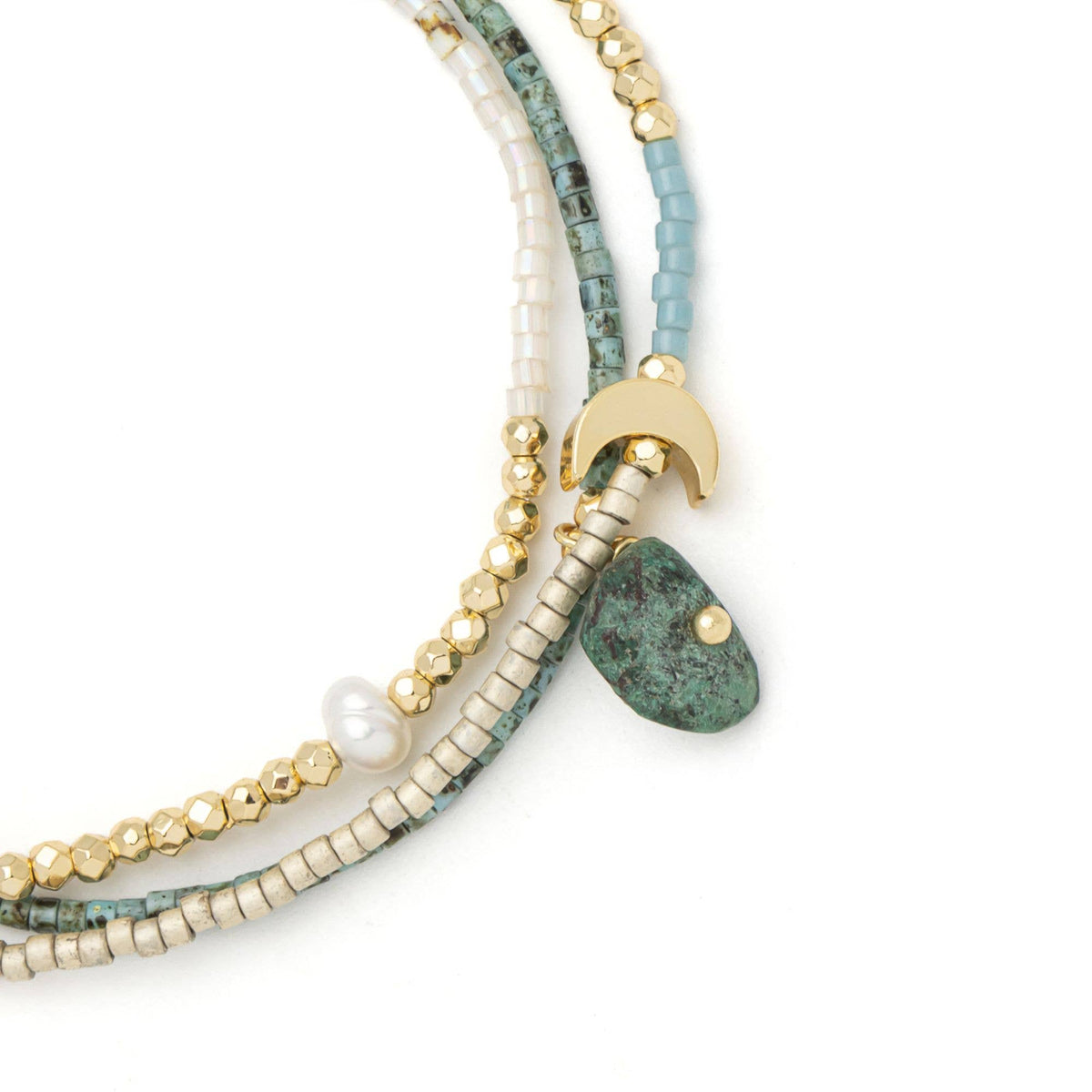 Scout Curated Wears’ Mixed Media Wrap Bracelet/Necklace – Transformation/African Turquoise features four vibrant strands adorned with gold, turquoise, white, and blue Miyuki beads. This versatile set includes an adjustable bracelet with a gold crescent charm, one accented by striking African Turquoise, and another finished with a delicate white pearl for an elegant touch.
