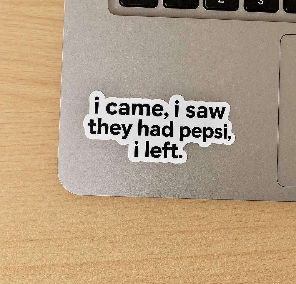 A laptop with a matte finish features the Funny “I came, I saw they had pepsi, i left” Sticker from Hello Brand | Sticker My Art, placed on a light wood desk.