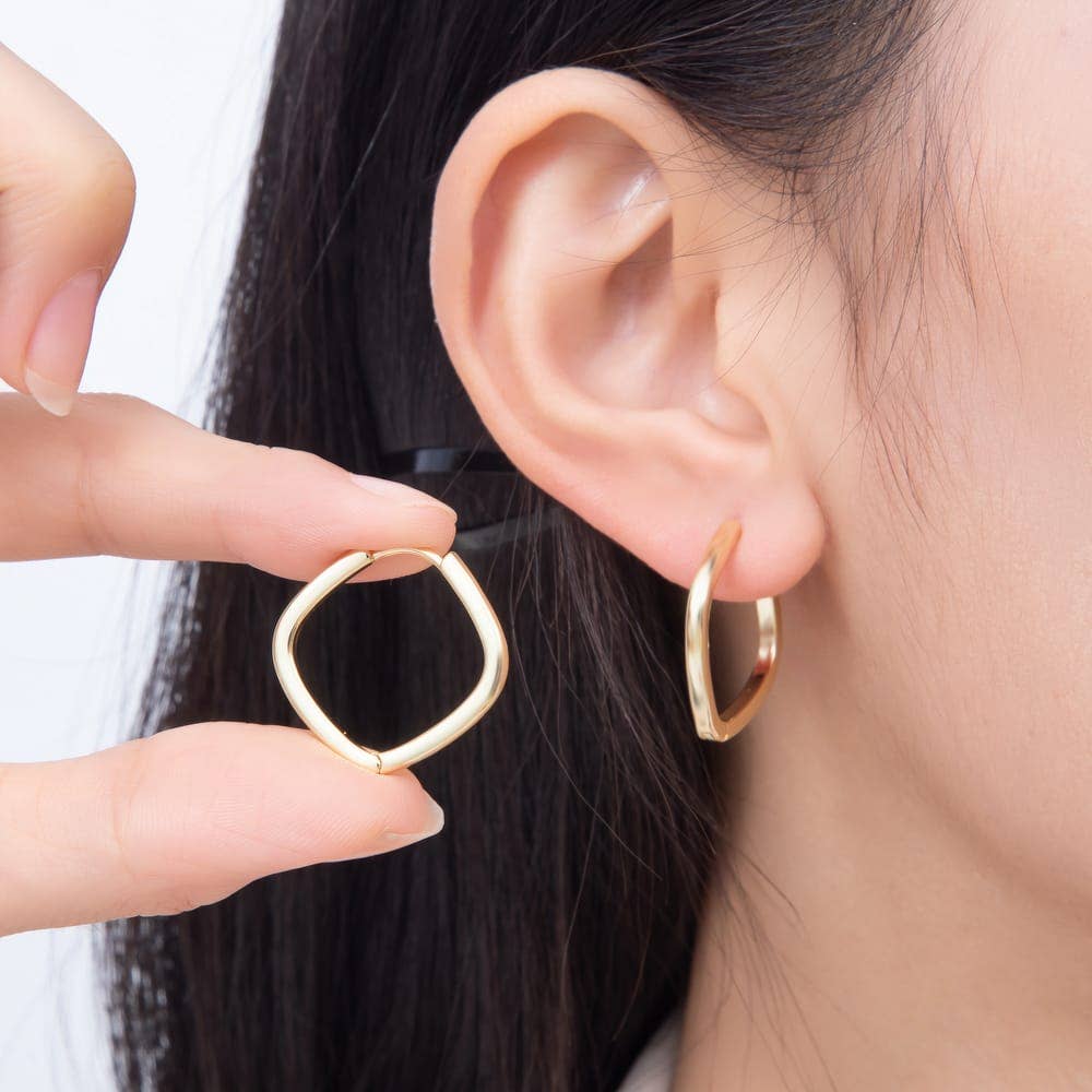 A hand holds a Gold Filled 25mm Square Huggie Hoop Earring next to one being worn on an ear.