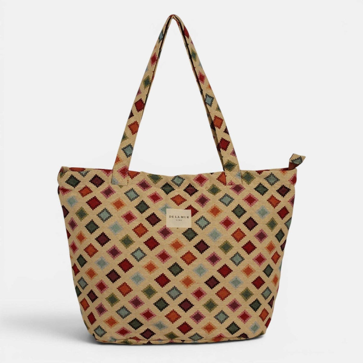 Introducing the Geometric Jacquard Large Zippered Tote Bag – Multicolor (Zac) by DE LA MUR LINE US Inc: A spacious jacquard tote with long handles, adorned with a striking geometric diamond pattern in red, yellow, blue, and black on a beige background. The design is finished with a small rectangular label centered on the front.