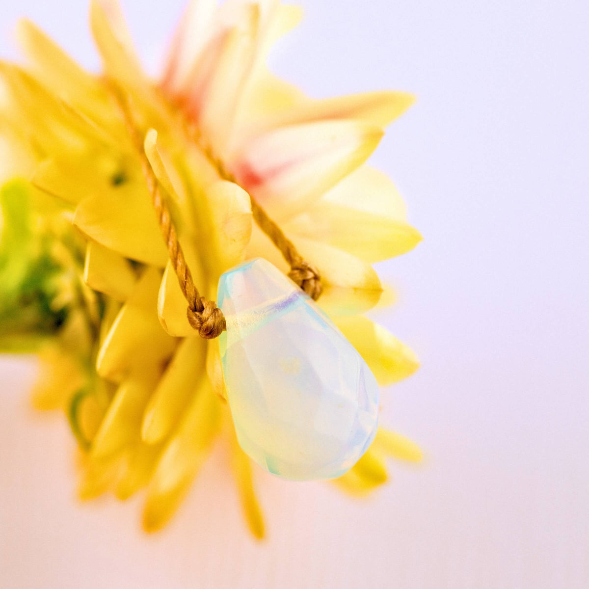 The Opaline Crystal Necklace Gift for Motherhood - Mom, Mother’s by SoulKu rests on yellow petals, its handmade opalescent pendant glowing softly—a stunning piece of gemstone jewelry.