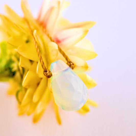 The Opaline Crystal Necklace Gift for Motherhood - Mom, Mother’s by SoulKu rests on yellow petals, its handmade opalescent pendant glowing softly—a stunning piece of gemstone jewelry.
