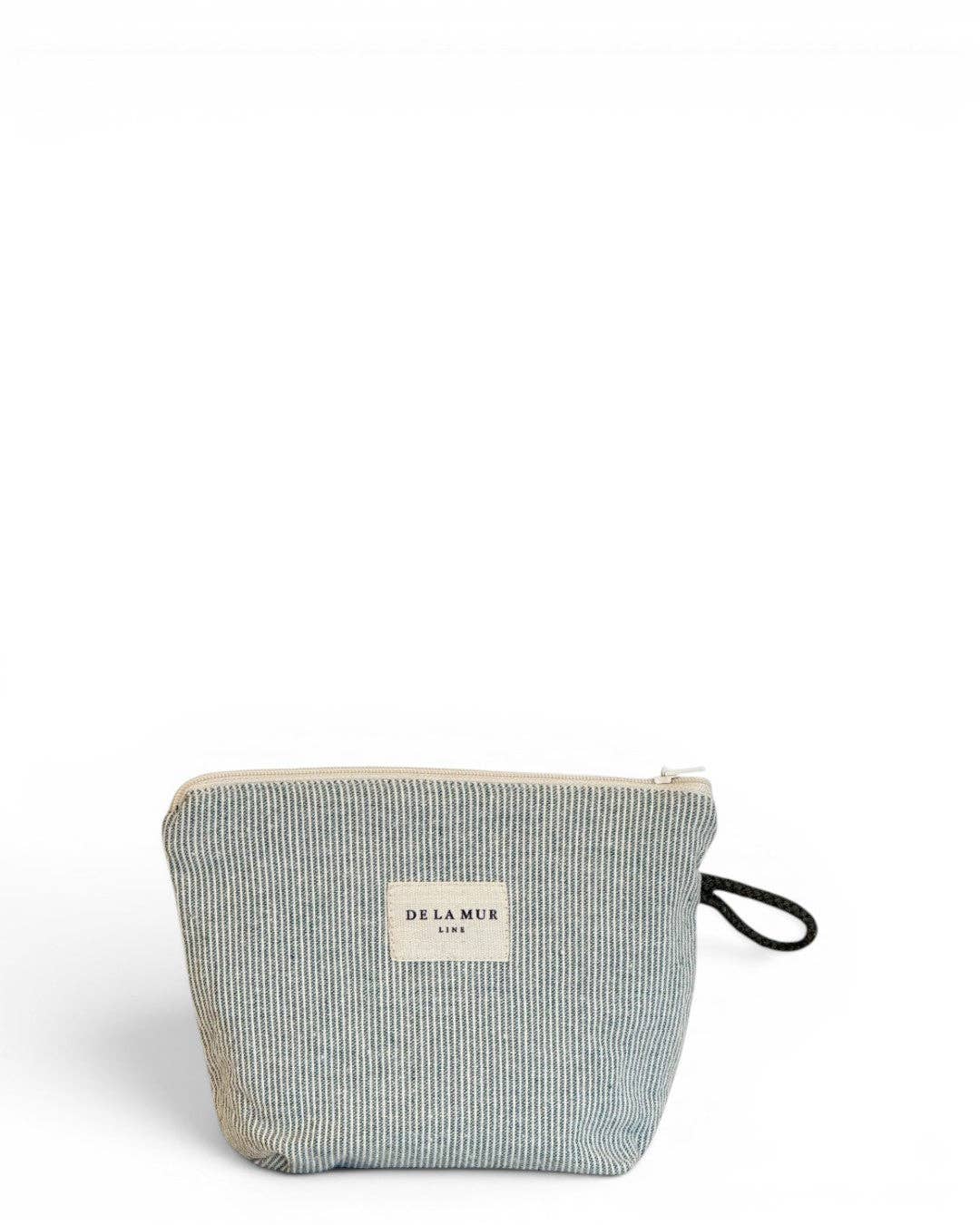A compact, light green and green striped zippered pouch crafted from jacquard fabric with a DE LA MUR LINE US Inc label on the front and a black wrist strap on the right side, set against a plain white background—perfect as a chic makeup bag made in Barcelona.
