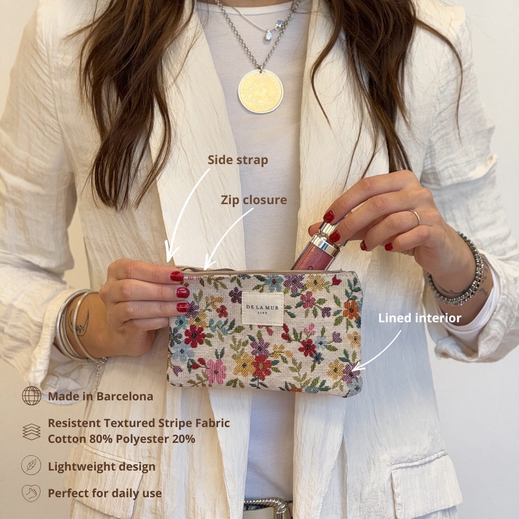 A woman in a white jacket holds the DE LA MUR LINE US Inc Floral Jacquard Small Makeup Bag / Coin Purse – Beige (Blum), displaying its side strap, zip closure, and lined interior. Text highlights features: made in Barcelona from jacquard fabric, lightweight construction, and perfect for daily use as a coin purse or compact makeup bag.